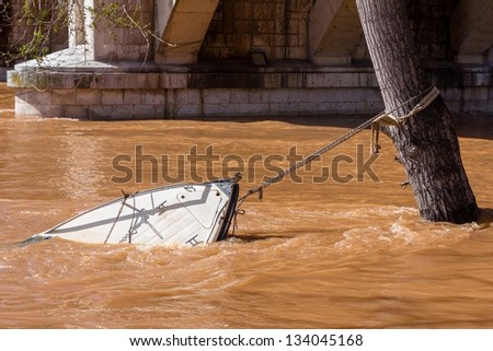 Sinking boat chained to a tree being dragged by the water.