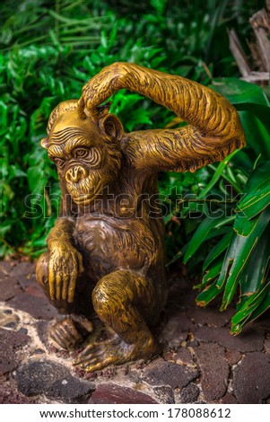 Golden chimpanzee statue surrounded by nature scratching its head.