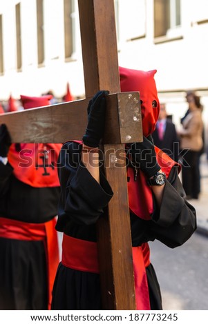 VALLADOLID, SPAIN - APRIL 17, 2014: Red and black nazareno carrying a wooden cross in the religious processions during Holy Week on Good Thursday, on April 17, 2014 in Valladolid, Spain.