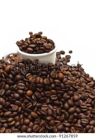 Upper view of a espresso cup buried with dark roasted coffee beans, on a coffee mountain with limited depth of field (shallow depth of field), isolated on white.