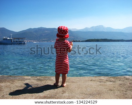 Little girl from behind dressed in stripy red skirt looking in to the sea