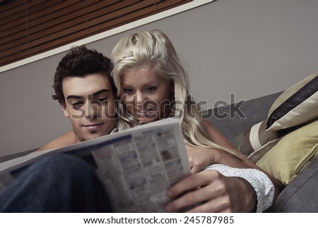 Happy couple sitting on the couch reading the newspaper