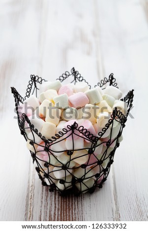 Colorful marshmallows in black wire basket, selective focus