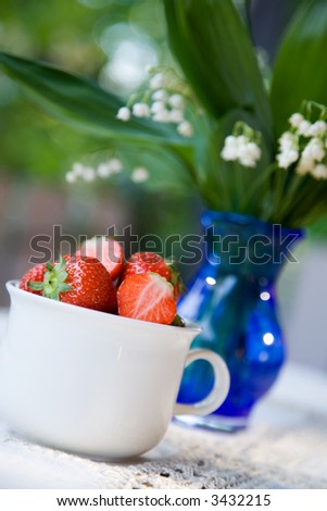 Strawberries in white cup and vase of lily of the valley