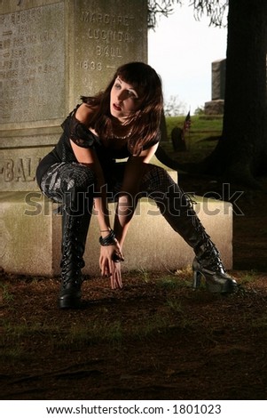 Goth girl sitting on grave stone.
