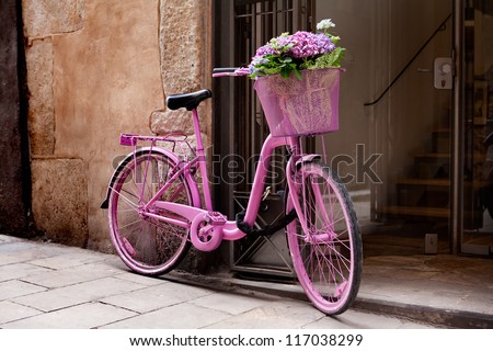 pink bicycle standing on the street - some flowers in the basket