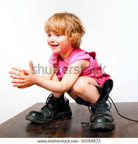 little girl in big boots standing on a table and clapping her hands