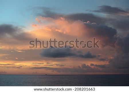 Clouds in the light of setting sun over calm sea and small ship