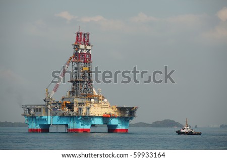 Floating drilling rig in the light of morning sun with attached tugboat