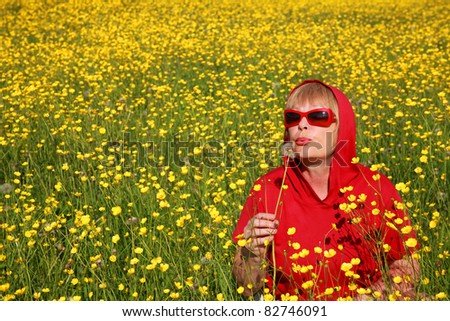 Romantic woman in red blouse in  her fifties  in the sunny meadow blowing on dandelion