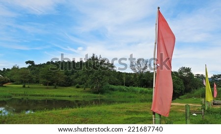 Pink and yellow flag with green natural grass land and blue sky background