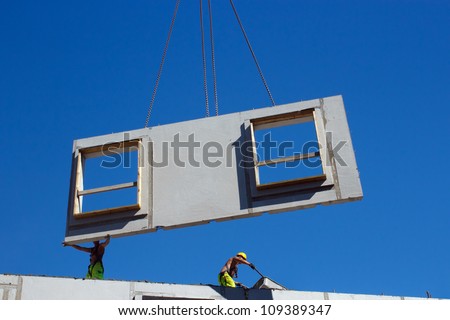 Installing precast concrete wall panel with crane and two workers in the construction site