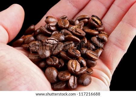 Fresh roasted coffee beans in hand, black background
