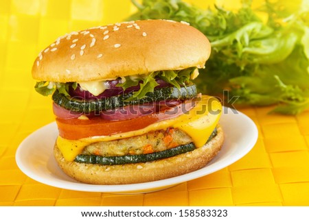 Veggie burger with vegetable patty , cheese , grilled zucchini , tomato and onion.  Lettuce in background.