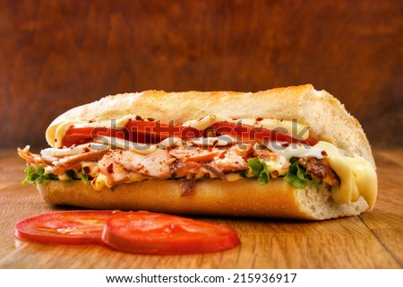 Hot smoked salmon submarine sandwich with tomato , mozzarella cheese , lettuce and mayonnaise on wooden surface