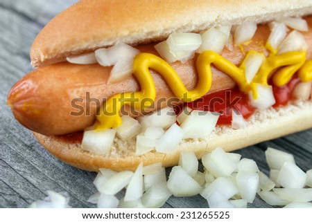 Hot dog closeup with yellow mustard and lot of minced onion on wooden board
