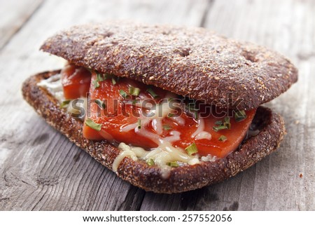 Hot rye bread sandwich with grilled sausage and cheese on gray wooden surface