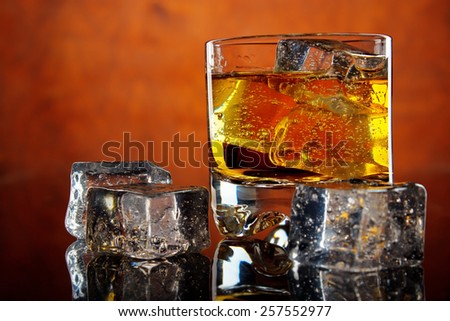 Glass of whiskey with ice cubes on dark reflective table , red background