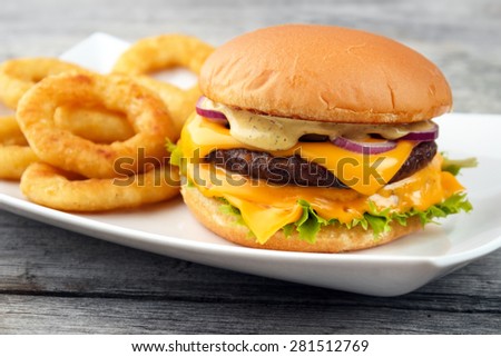 Cheeseburger served with deep fry onion rings on the white square dish and wooden board background