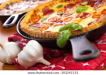 Cast iron skillet pan pizzas with garlic bulbs on wooden table closeup