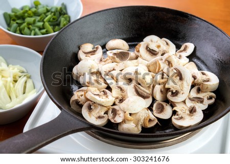 Sliced champignon mushrooms on cast iron skillet ready to cook mushroom sauce , chopped onions and chives on left