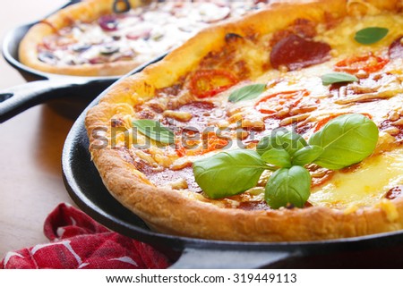 Cast iron skillet pan pizzas on wooden table closeup