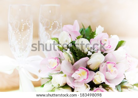 Two glasses of champagne and a beautiful tender festive wedding bouquet of flowers, buttercups and white lilac on a white painted wooden board.