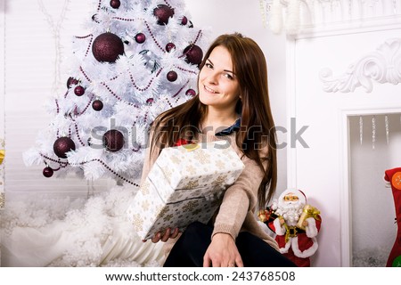 Beautiful girl with gift sitting by the fireplace and christmas tree