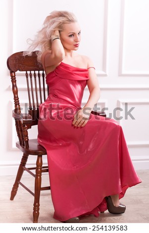 sexy sensual blonde woman in red dress with long hair sitting on the chair