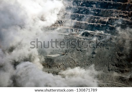 excavators,trucks and heavy machinery in open cast mine after blast among dust and smoke