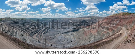 panorama of quarry extracting iron ore with heavy trucks, excavators, diggers and locomotives