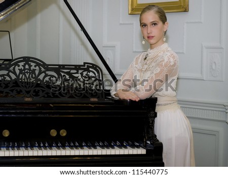 Beautiful girl dressed in a period costume rests on a grand piano