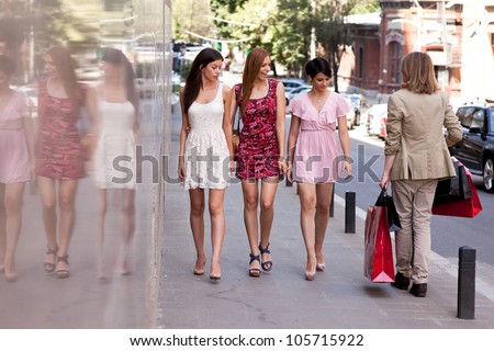 Group of three young beautiful women looking after a hansome man with many shopping bags walking on the street.