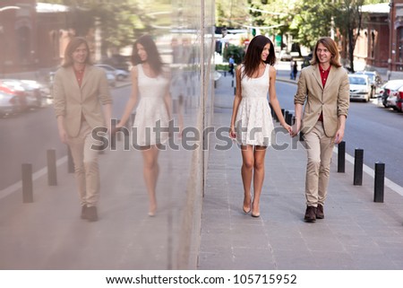 Fashionable happy young couple of a handsome man with long hair and attractive woman walking on the street holding hands