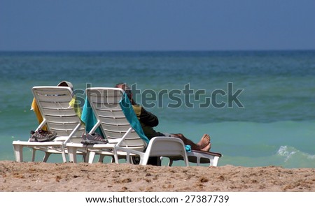 Rear view of a couple relaxing on lounge chairs looking at the ocean