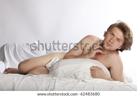 Portrait of a naked man in bed, hiding behind a pillow. Studio shot. See more in my portfolio