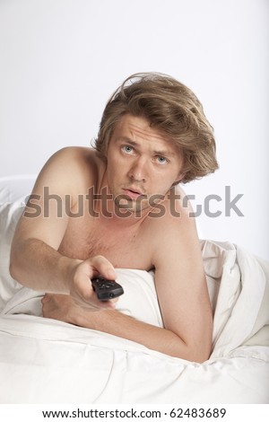 Portrait of a scared young man lying in bed watching horror movies. Studio shot. See more in my portfolio