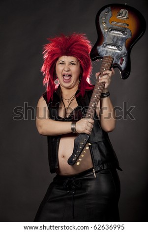 Pregnant sexy woman acting as rock star with red rumpled wig, leather clothes and electrical guitar. Concept image for fun and extreme during pregnancy. Studio shot. See more in my portfolio