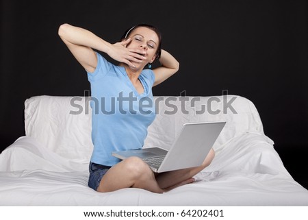 Tired young business woman on bed with  a laptop, yawning. Part of photo series. Studio shot