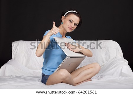 Happy young business woman on bed with  a laptop, gesturing ok sign. Part of photo series. Studio shot