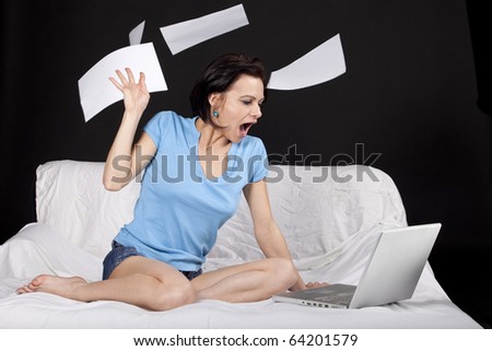 Shocked young business woman on bed with  a laptop and flying paper sheets. Part of photo series. Studio shot
