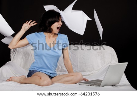 Happy young business woman on bed with  a laptop and flying paper sheets. Part of photo series. Studio shot