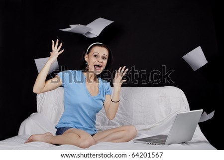 Happy young business woman on bed with  a laptop and flying paper sheets. Part of photo series. Studio shot