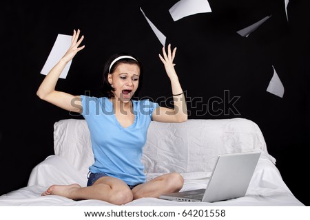Young angry business woman on bed with  a laptop and flying paper sheets. Part of photo series. Studio shot