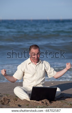 Young businessman at the beach with his laptop happy about success