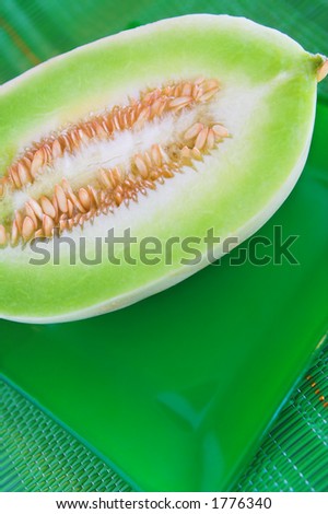 A melon cut in half on a green plate and placemat.