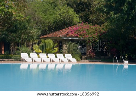 Swimming pool with chaise longues and old house at the far end, reflecting in the water.