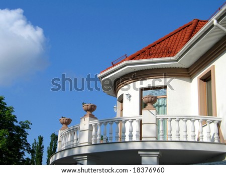 Upper class luxury home with a white fence surrounding it. There\'s a deep blue sky in the background.