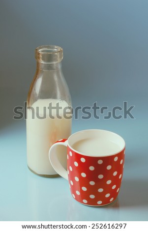 Vintage still life with red, in polka dot, cup of milk and antique bottle of milk on a blue background.