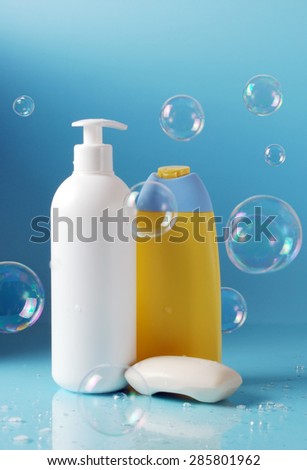 cosmetic bottles and solid soap with soap bubbles in front of blue background